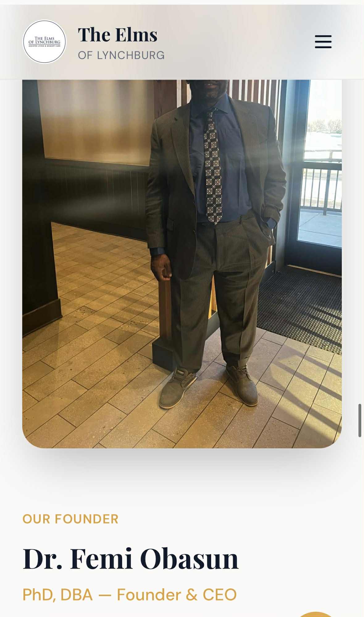 Person in suit standing indoors with tiled floor and window in background.