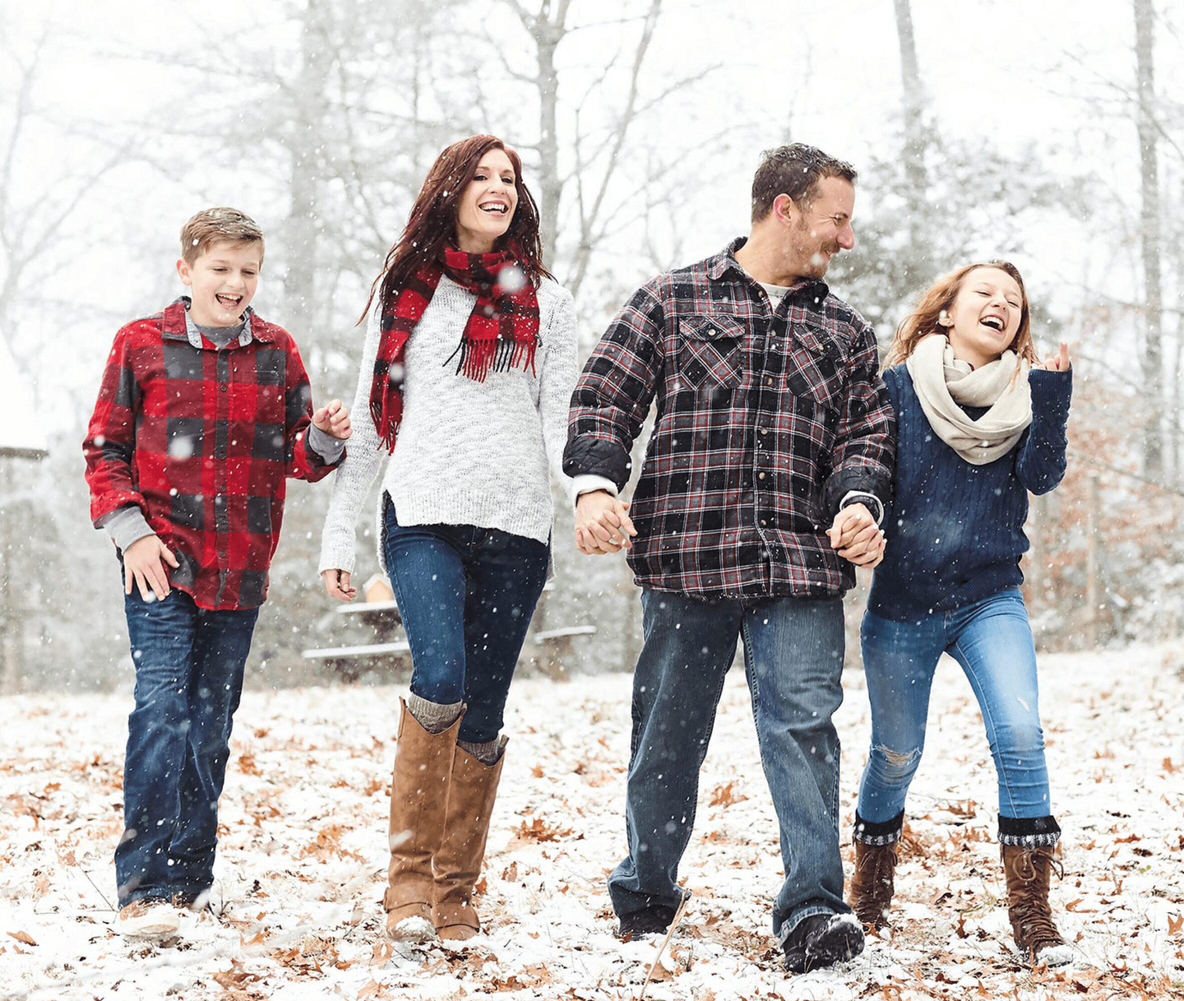 Family of five walking outdoors in a snowy forest, holding hands and smiling, dressed in winter clothing.