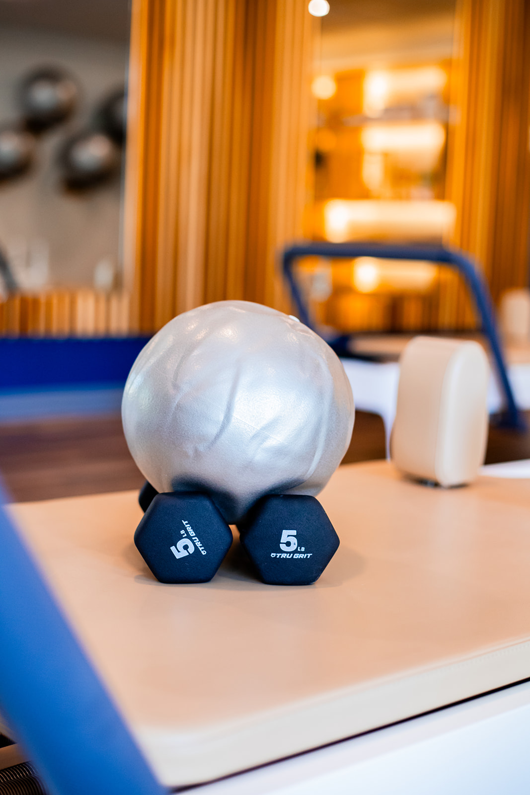 Dumbbells and a large white ball on a table in a gym, with wooden wall and exercise equipment in background.