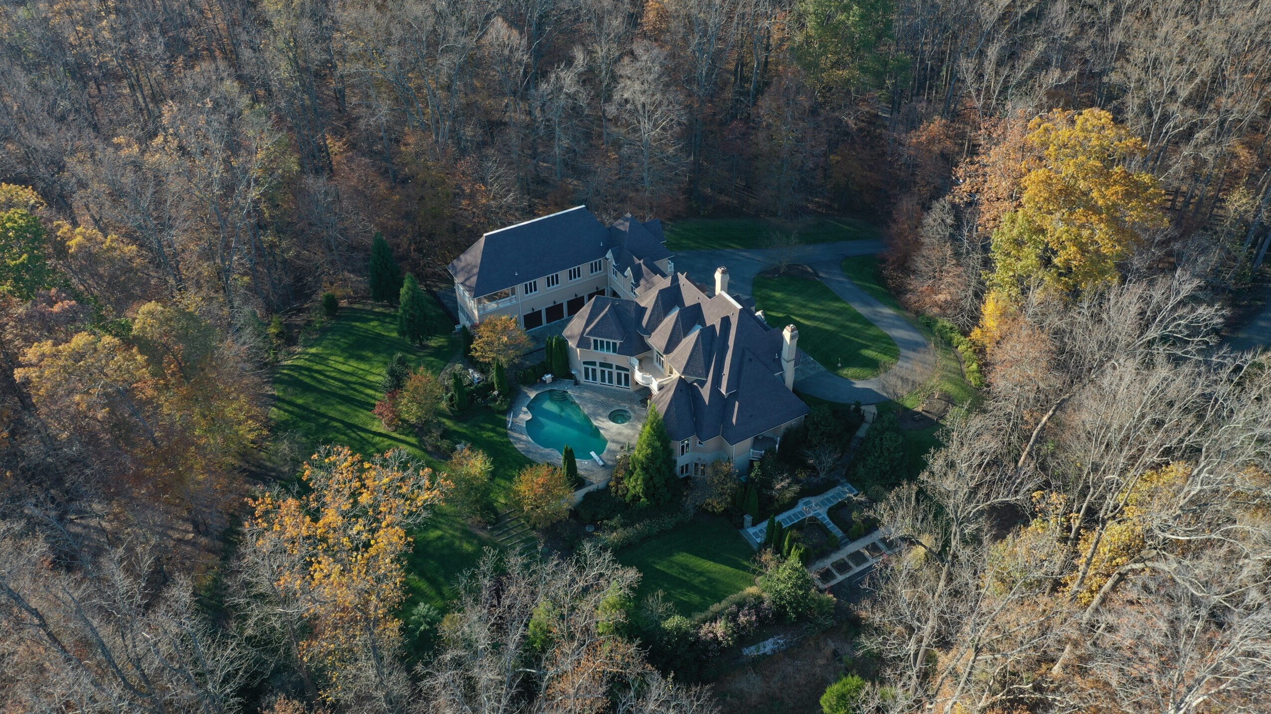 A large house with a pool surrounded by trees in a wooded area, viewed from above.