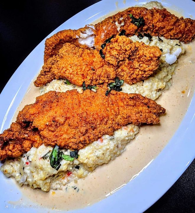 Three fried fish fillets on mashed potatoes with gravy, garnished with herbs, served on a white oval plate.