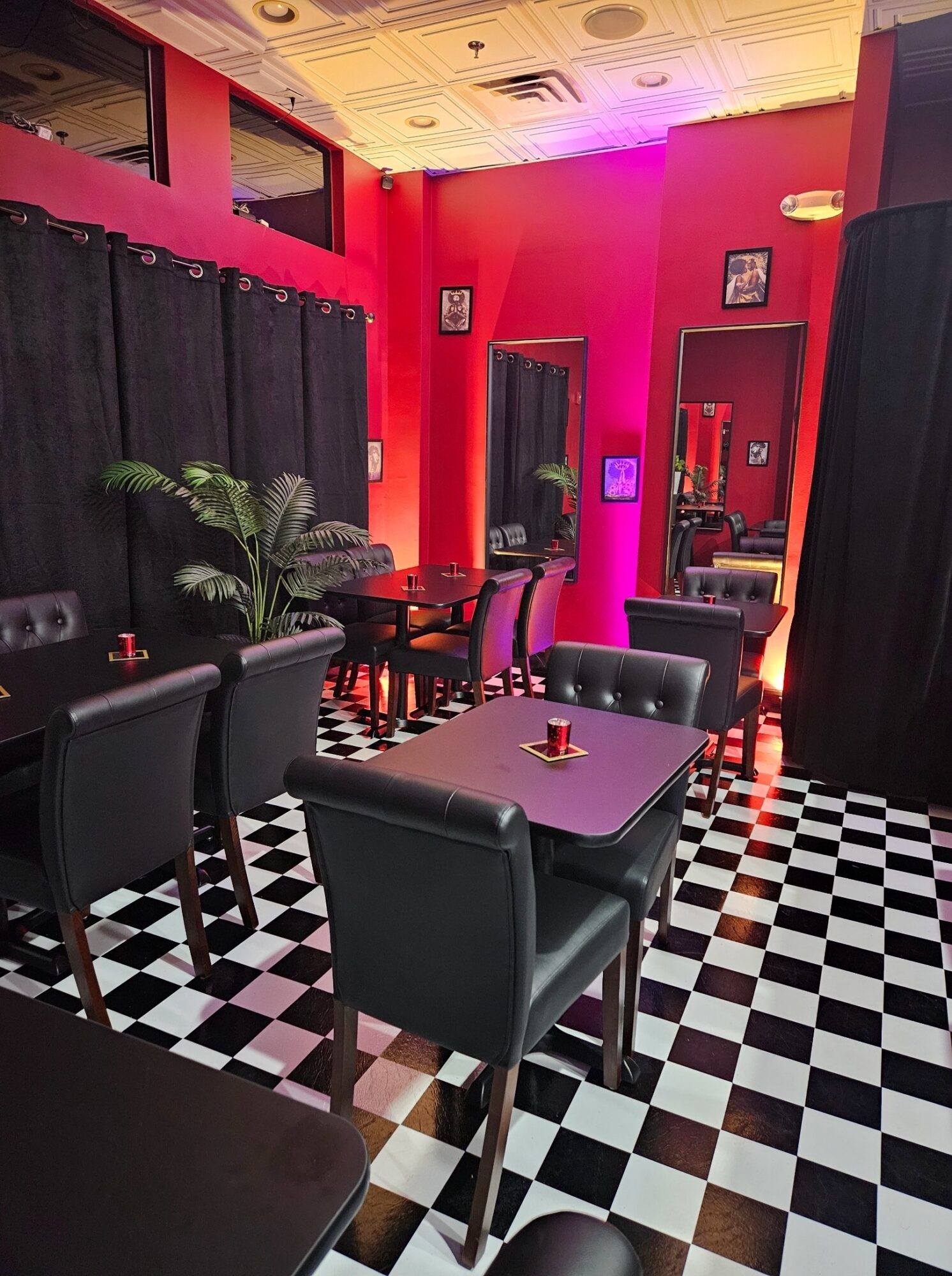 Interior of a vibrant pink-themed cafe with black and white checkered floor, black chairs, and pink walls, illuminated by colorful lighting.