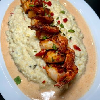 Grilled shrimp on creamy rice with herbs and red pepper flakes on a white plate.