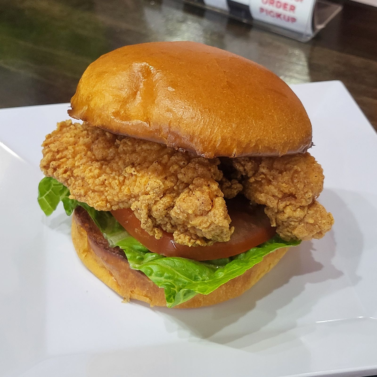 Fried chicken sandwich with lettuce, tomato, and bun on a white plate.