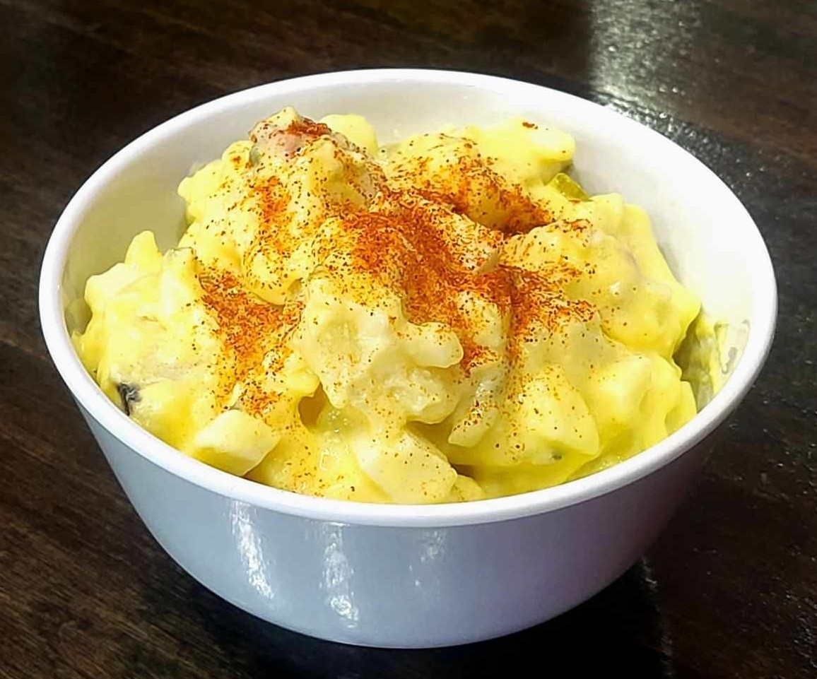 Bowl of potato salad topped with paprika on a dark wooden surface.