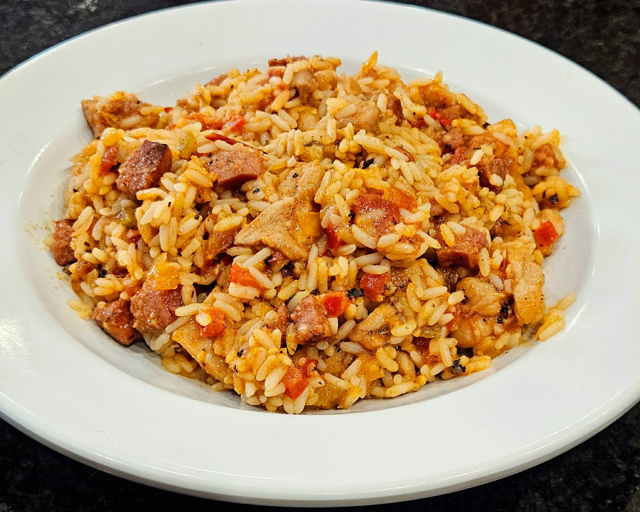 Plate of fried rice with vegetables and meat on a white dish, black background.