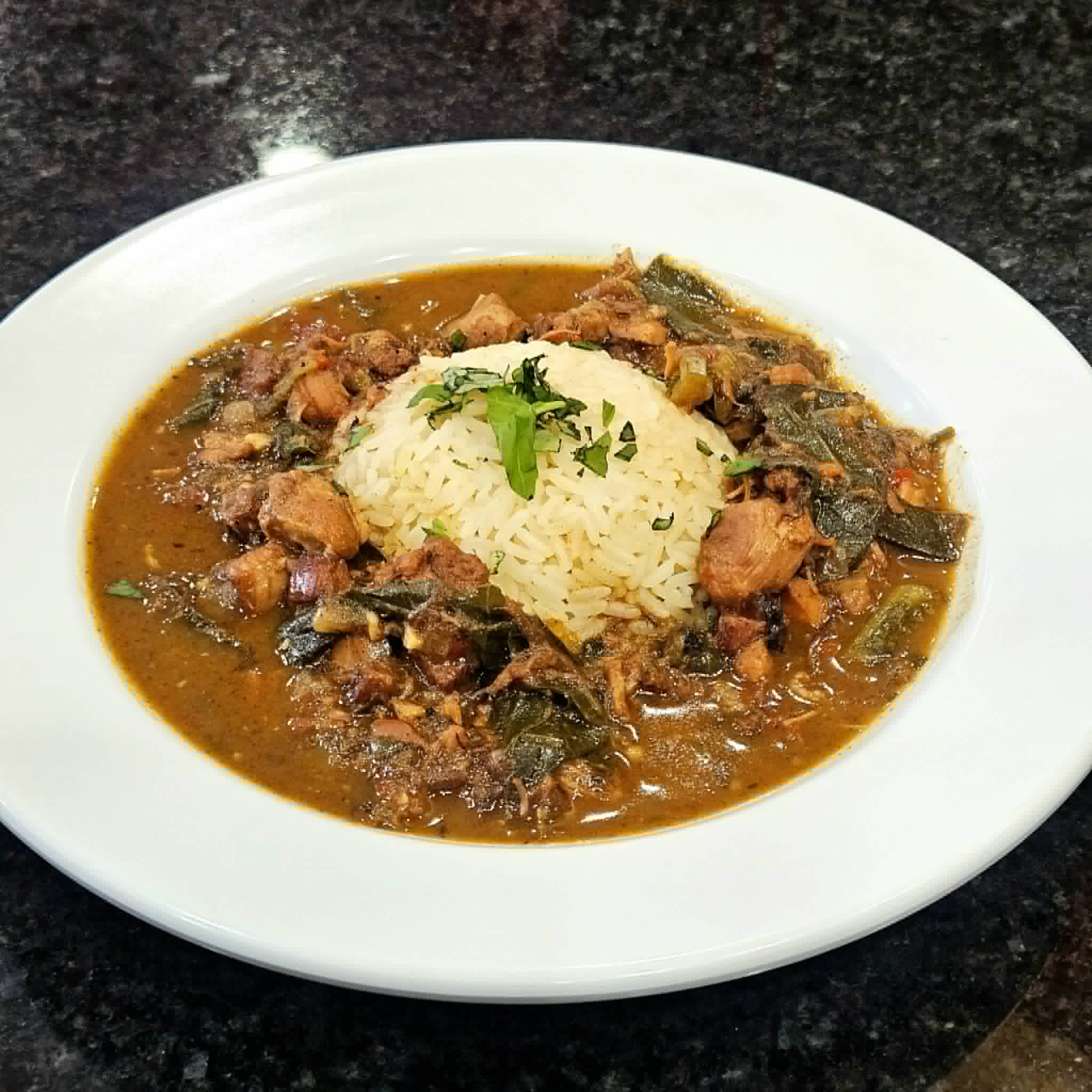 Plate with rice and vegetable stew garnished with cilantro on a black surface.