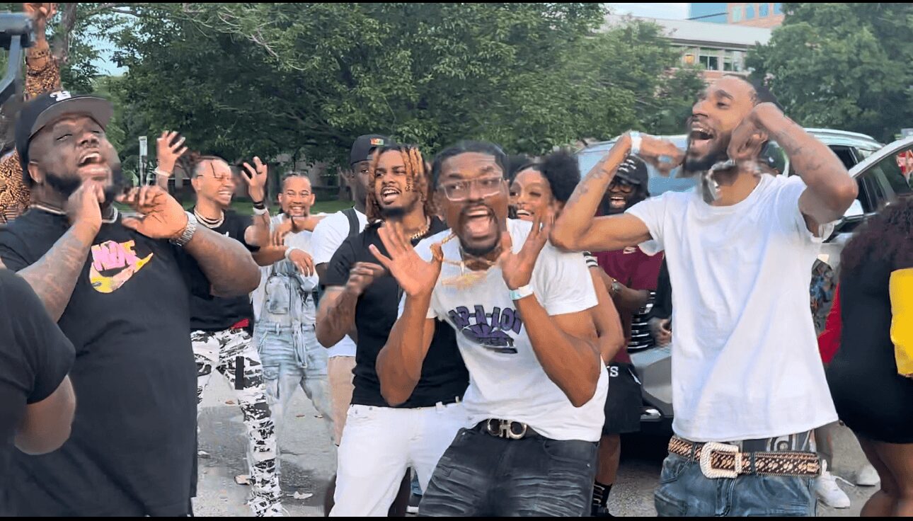 Group of people outdoors laughing and enjoying themselves, some with hands raised or covering ears.