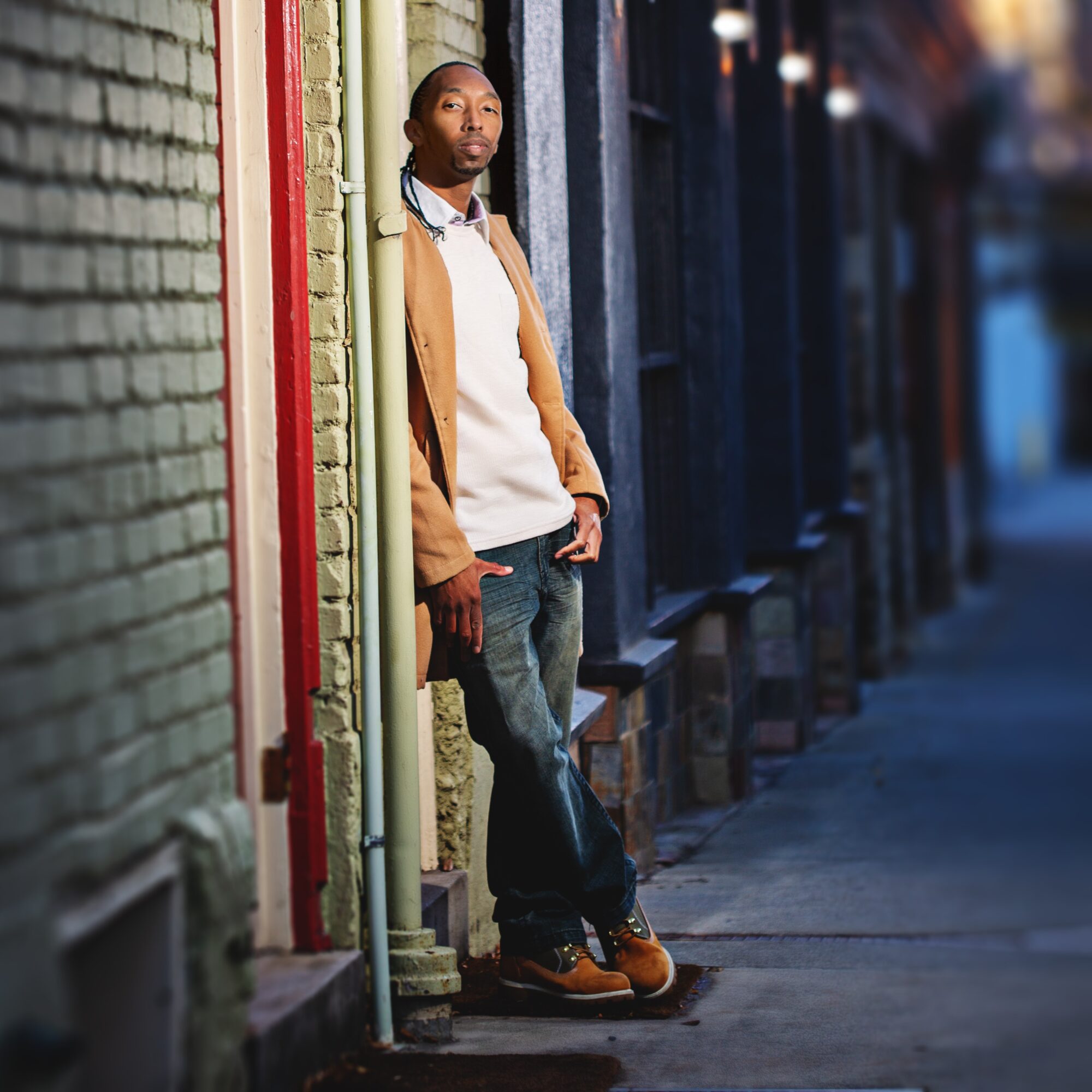 Person leaning against a colorful wall on a city sidewalk, looking to the side, with buildings in the background.