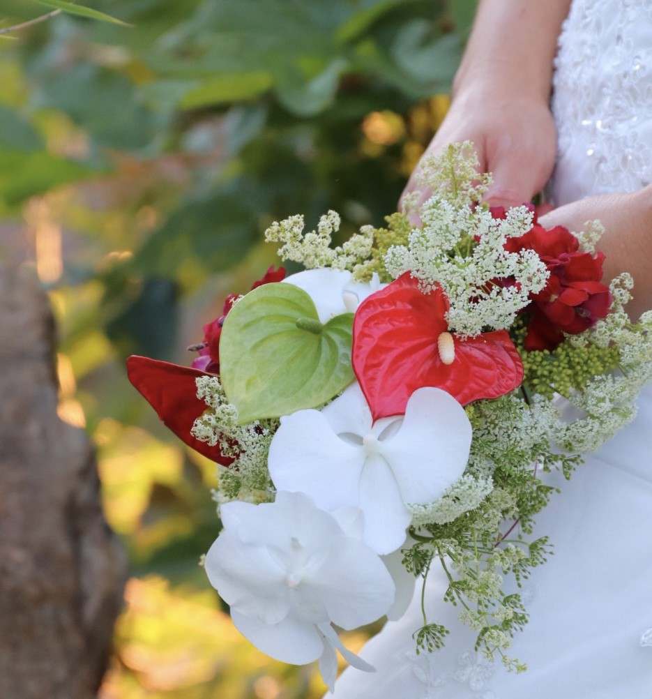 Person holding a bouquet of white, red, and green flowers, with a blurred outdoor background.
