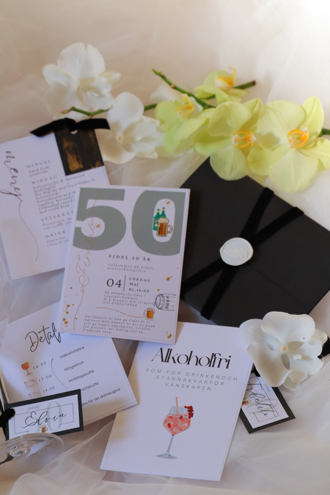 A black clock with white hands surrounded by white and yellow orchids, and various papers and cards on a light surface.