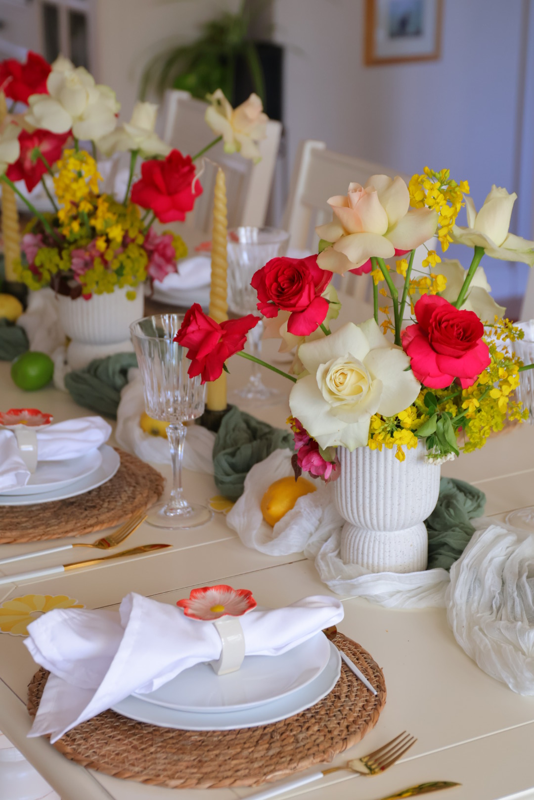 Table setting with floral arrangements, plates, napkins, and glasses, decorated with colorful flowers and greenery.