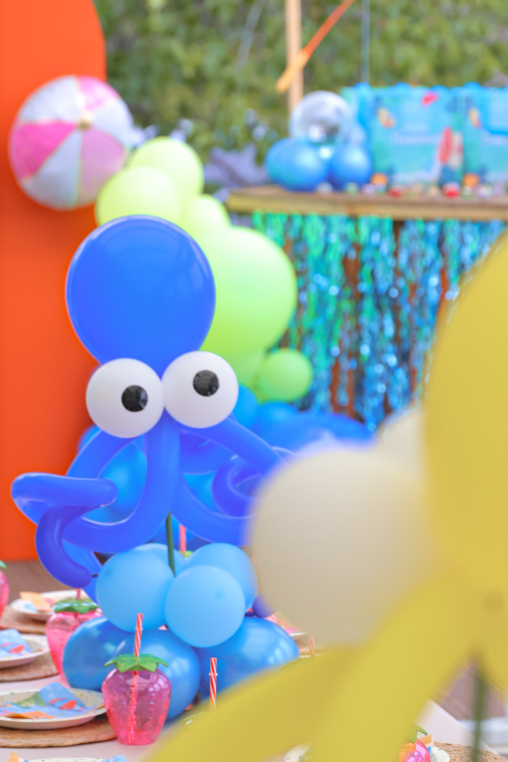 Colorful outdoor party with balloons, a blue octopus decoration, and a table with treats and decorations.