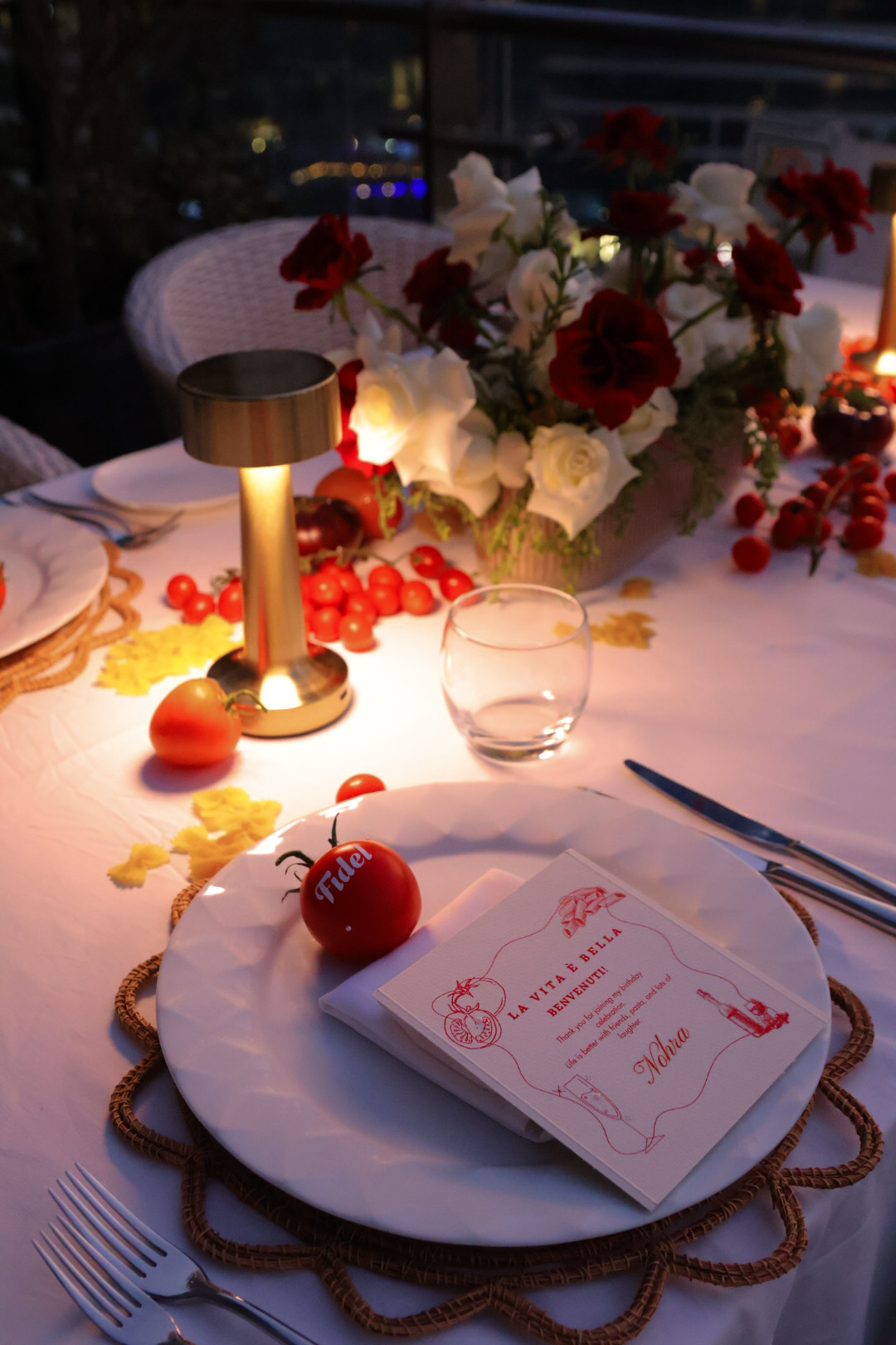 Table setting with a floral centerpiece, candle, glass, and a menu on a white plate, decorated with red berries and apples.
