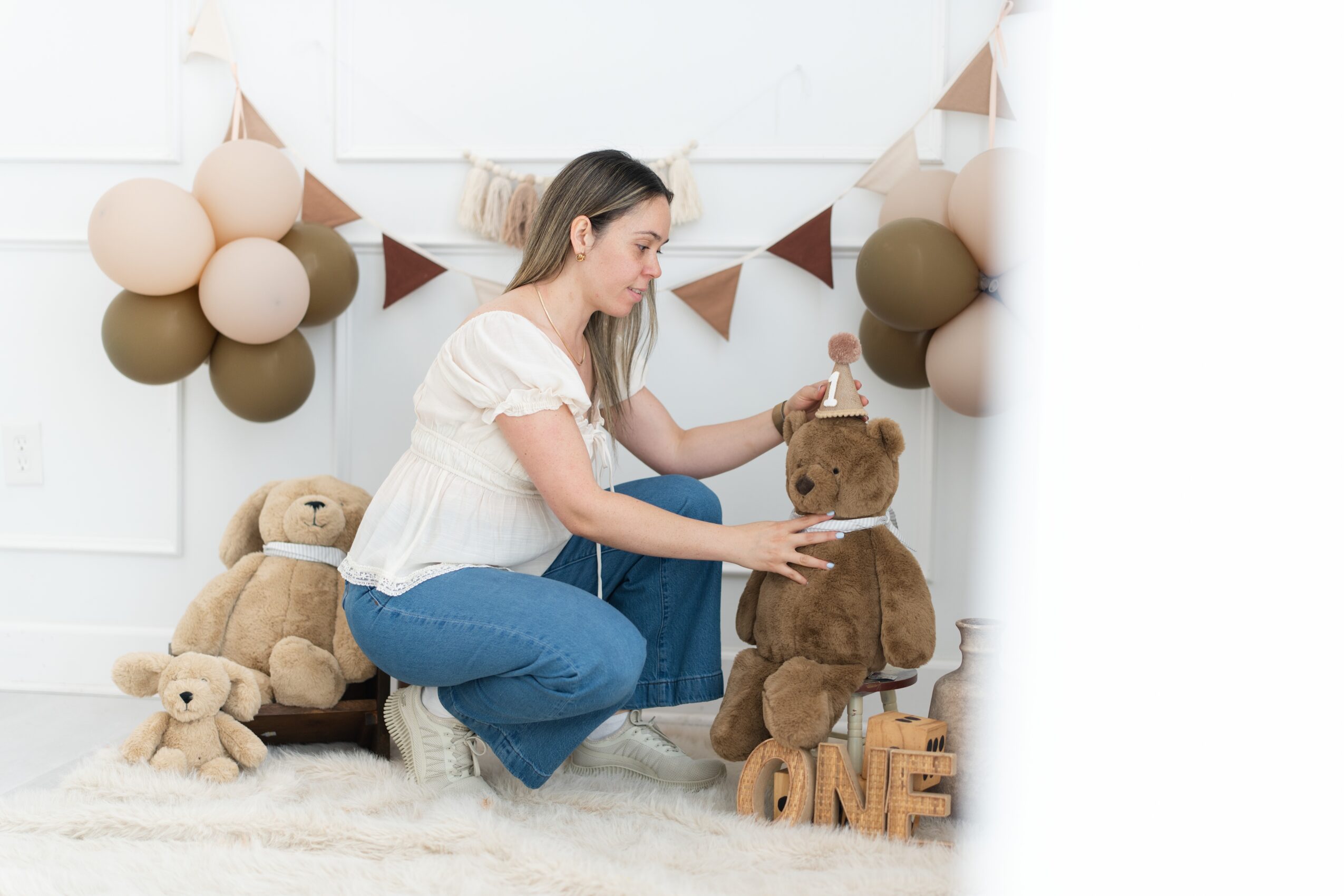 Woman sitting on the floor with stuffed animals and decorations behind her, holding a large teddy bear. 20 words.