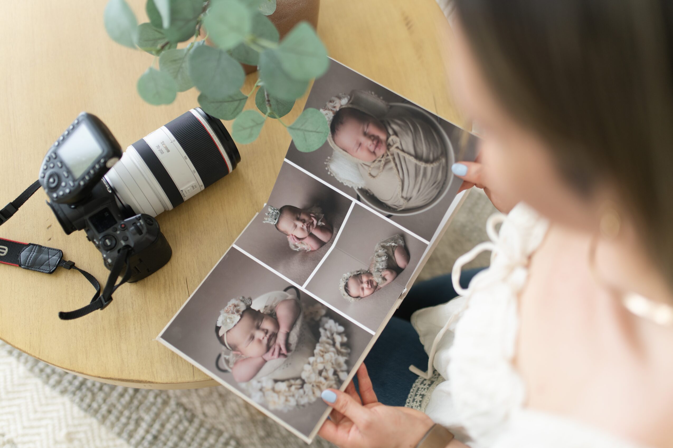 Person holding a photo sheet with six images of a young girl, on a wooden table with a camera and plant nearby.