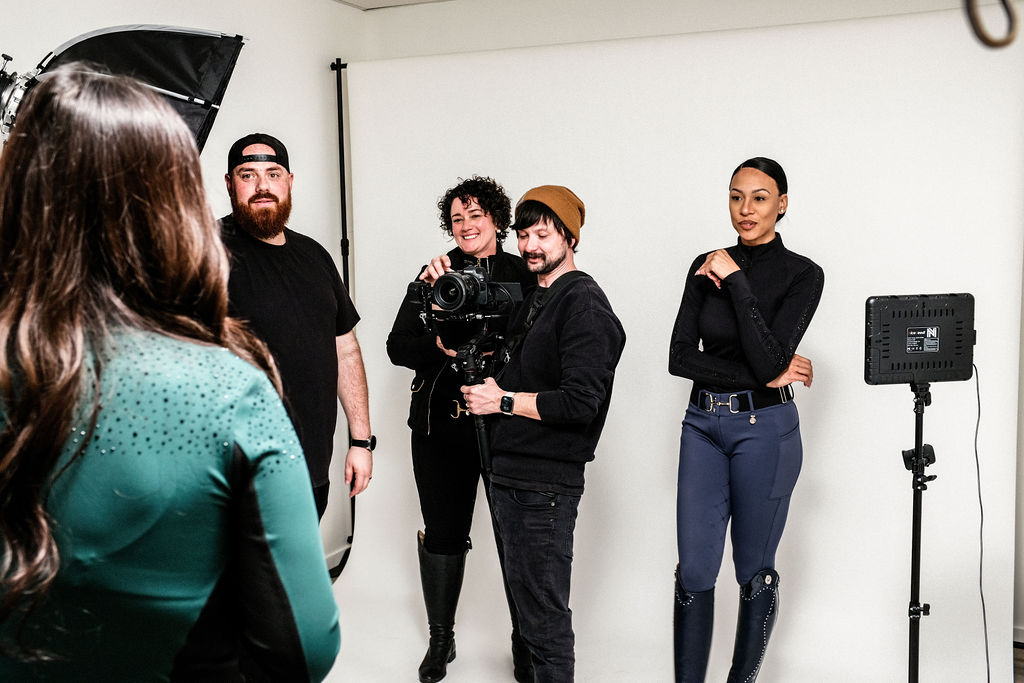 Group of five people in a photo studio, some holding cameras, with a white background and lighting equipment.