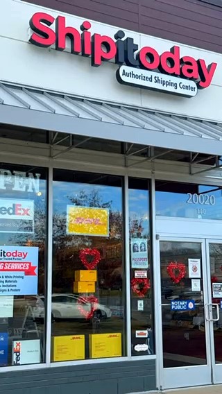 Ship it today store sign above entrance with glass doors and windows, reflections, and holiday decorations on the door handles.