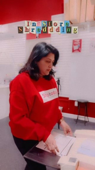Person with dark hair wearing a red sweater, standing at a table with books, in a classroom setting.