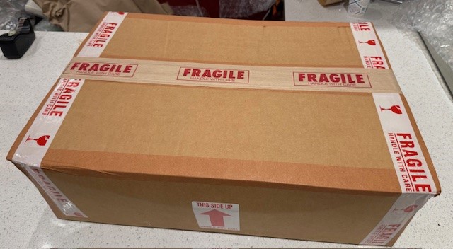 Closed cardboard box sealed with fragile tape on a table, with labels and markings.