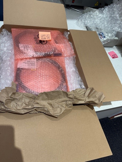 Open cardboard box with pink packaged item inside, surrounded by packing materials, on a white surface.