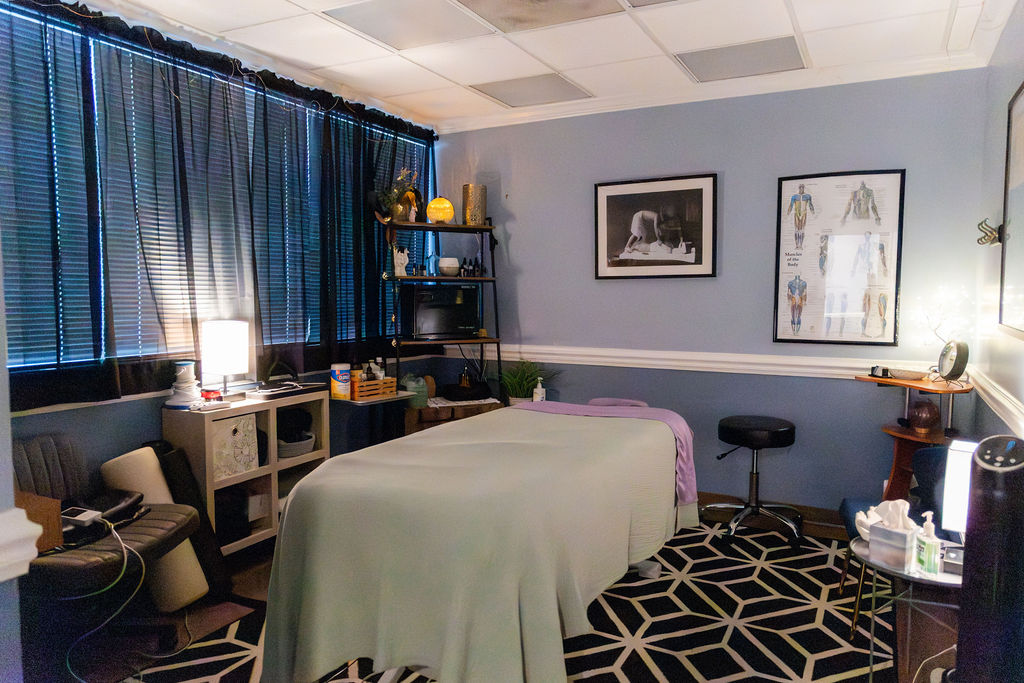 A room with a massage table covered with a white sheet, black and white patterned rug, and blue walls with framed pictures.