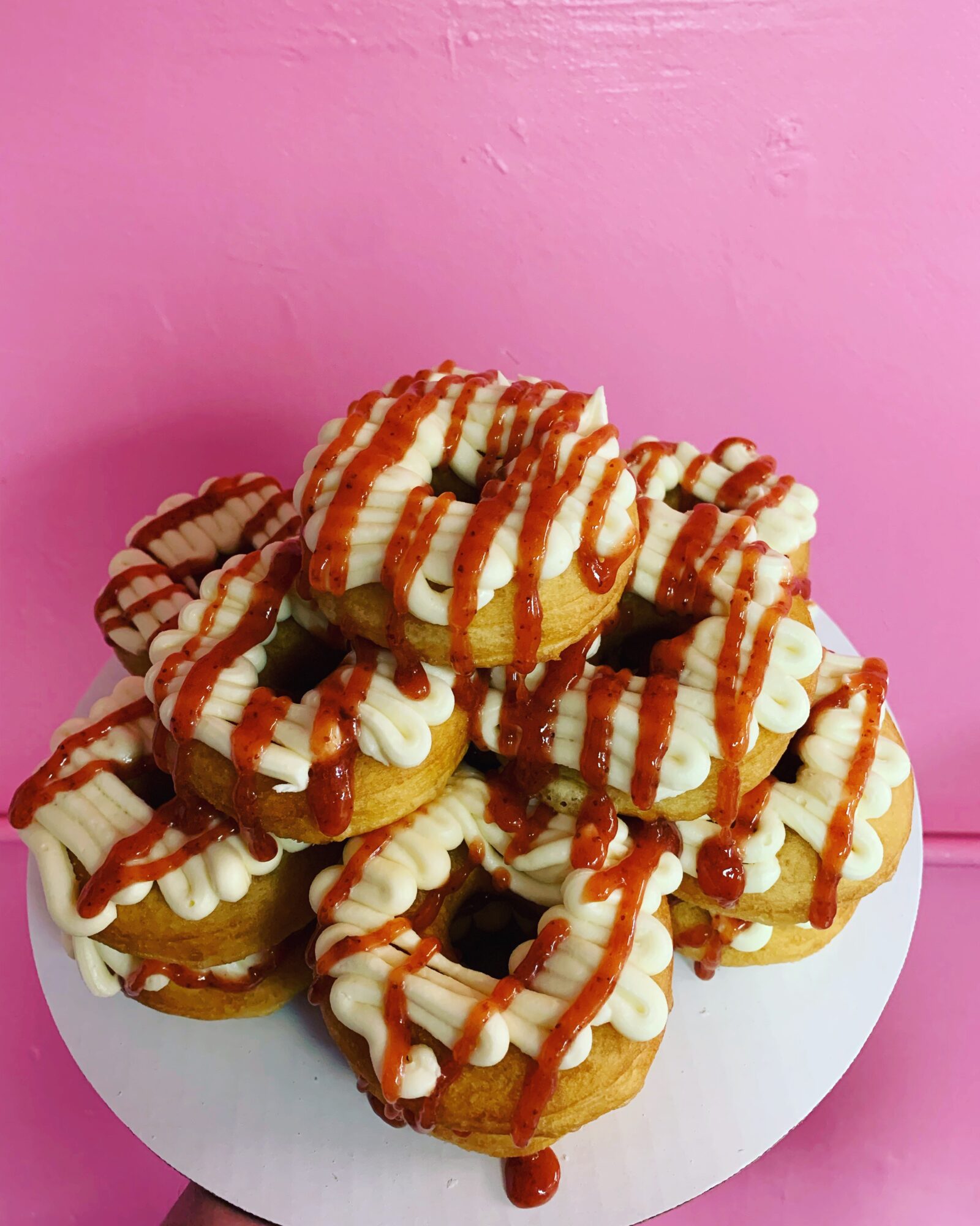 Plate of assorted donuts with icing and caramel drizzle against pink background.