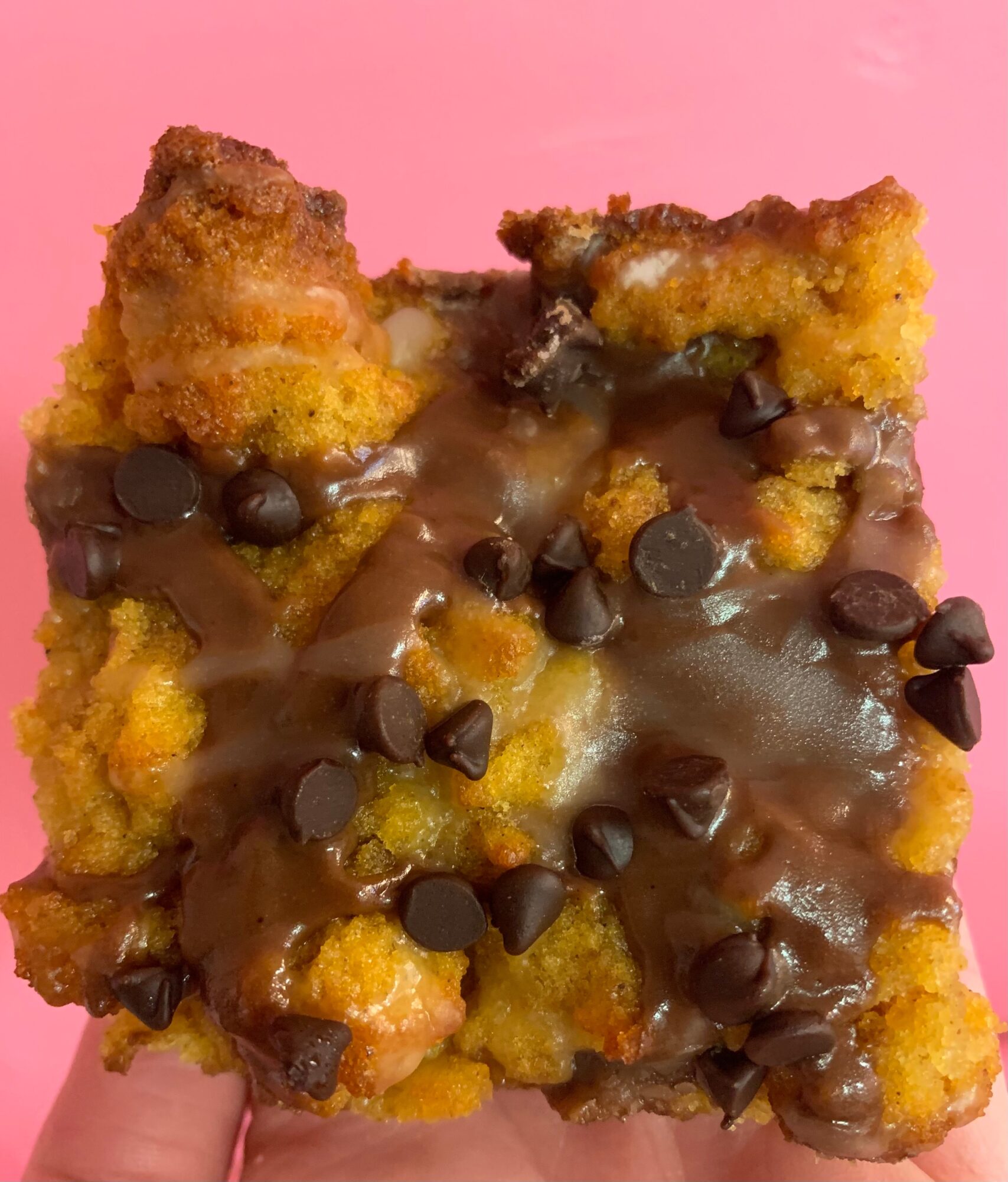 Close-up of a dessert with chocolate chips and caramel sauce on a pink background.