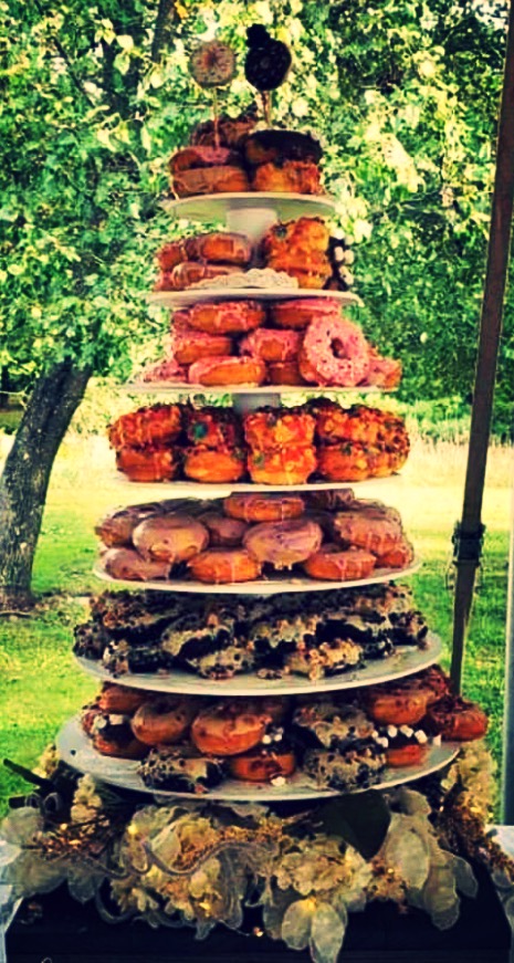 A multi-tiered dessert display with various pastries and sweets outdoors, surrounded by green trees and grass.