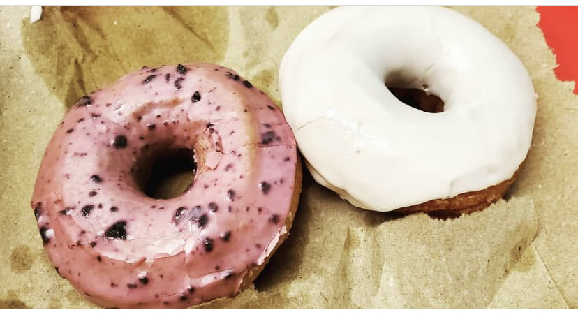 Two donuts, one pink with sprinkles and one white, on brown paper.