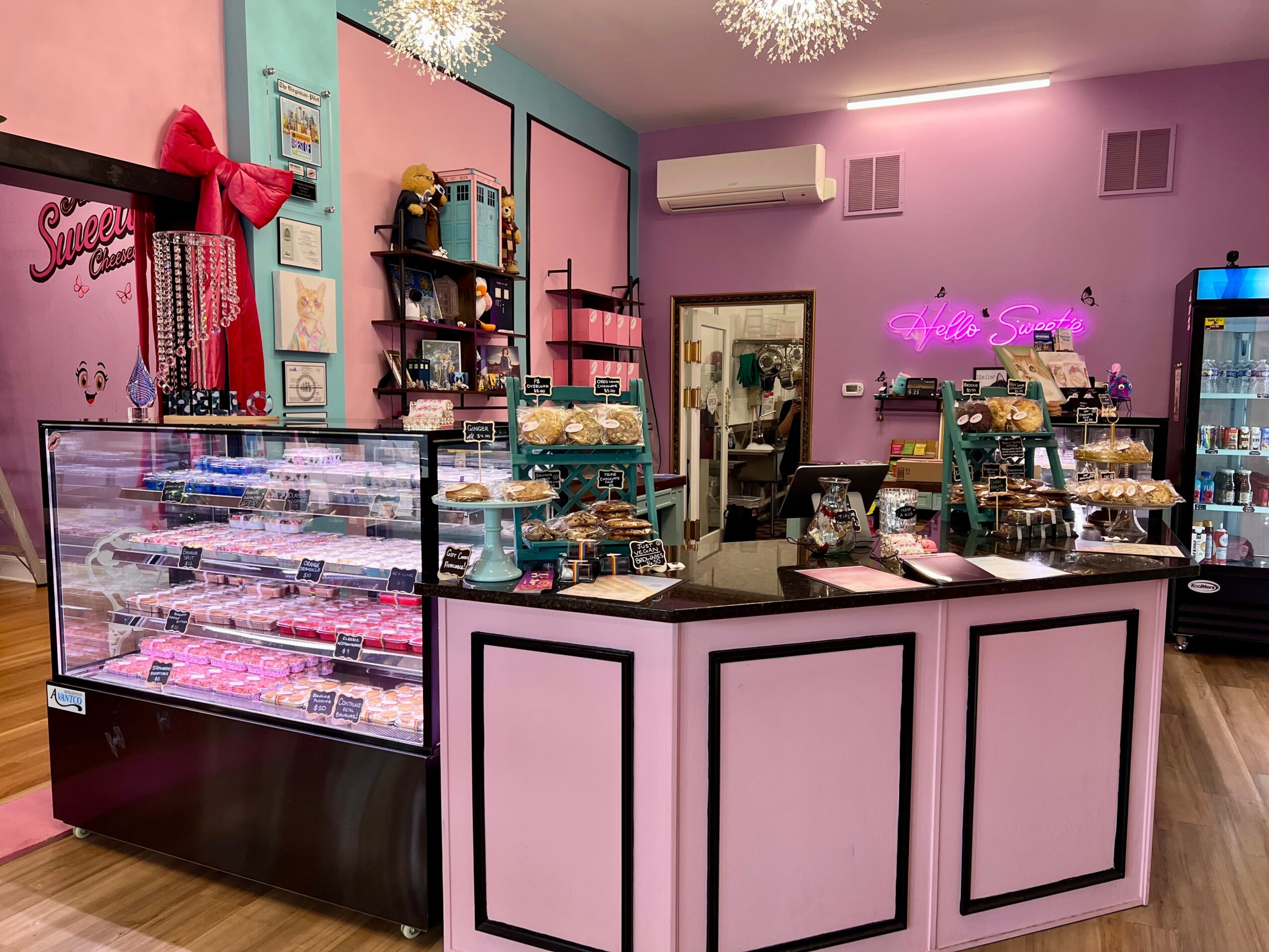 Interior of a boutique with pink and purple walls, display cases, shelves with jewelry, and a neon sign, with wooden flooring.