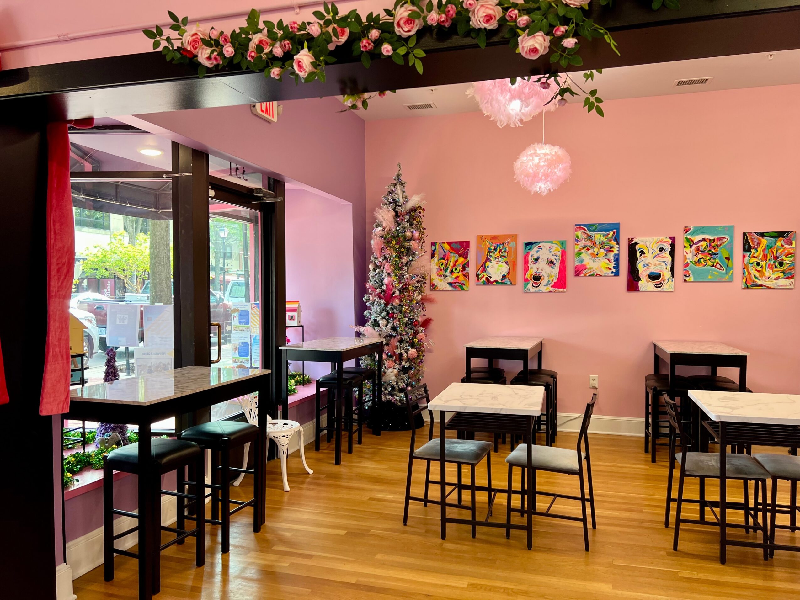 Interior of a decorated room with pink walls, a Christmas tree, colorful artwork, and tables with chairs.