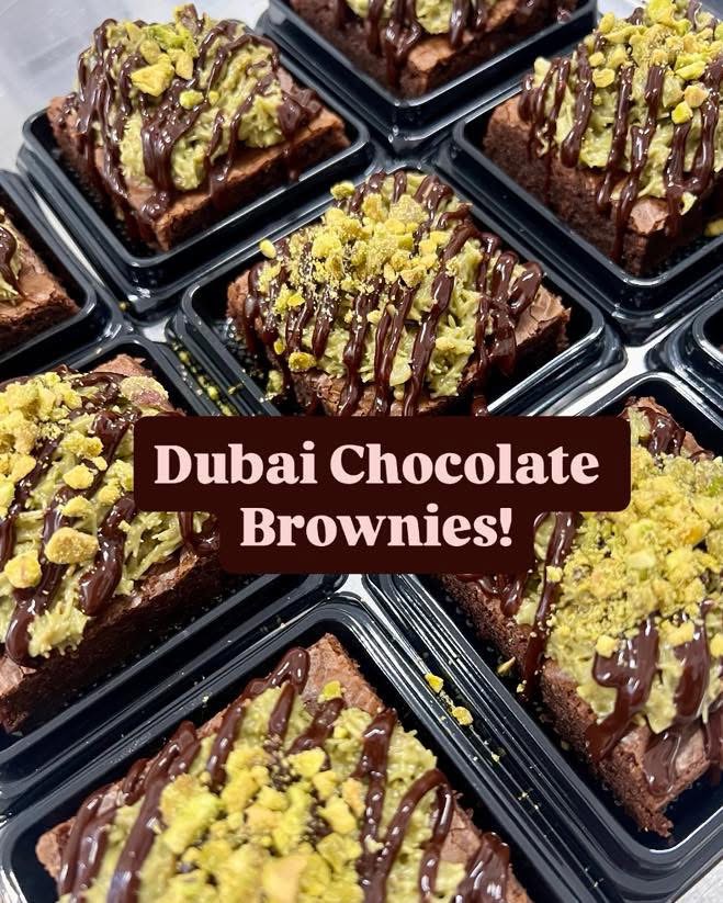 Multiple Dubai chocolate brownies topped with yellow crumbs and drizzled with chocolate, arranged in black trays.