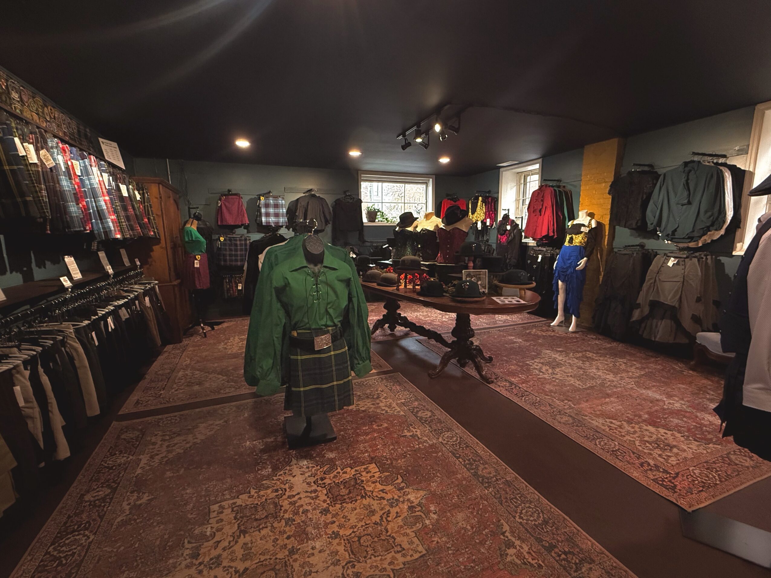 People shopping in a clothing store with racks of clothes on walls and mannequins, carpeted floor, and ceiling lights.