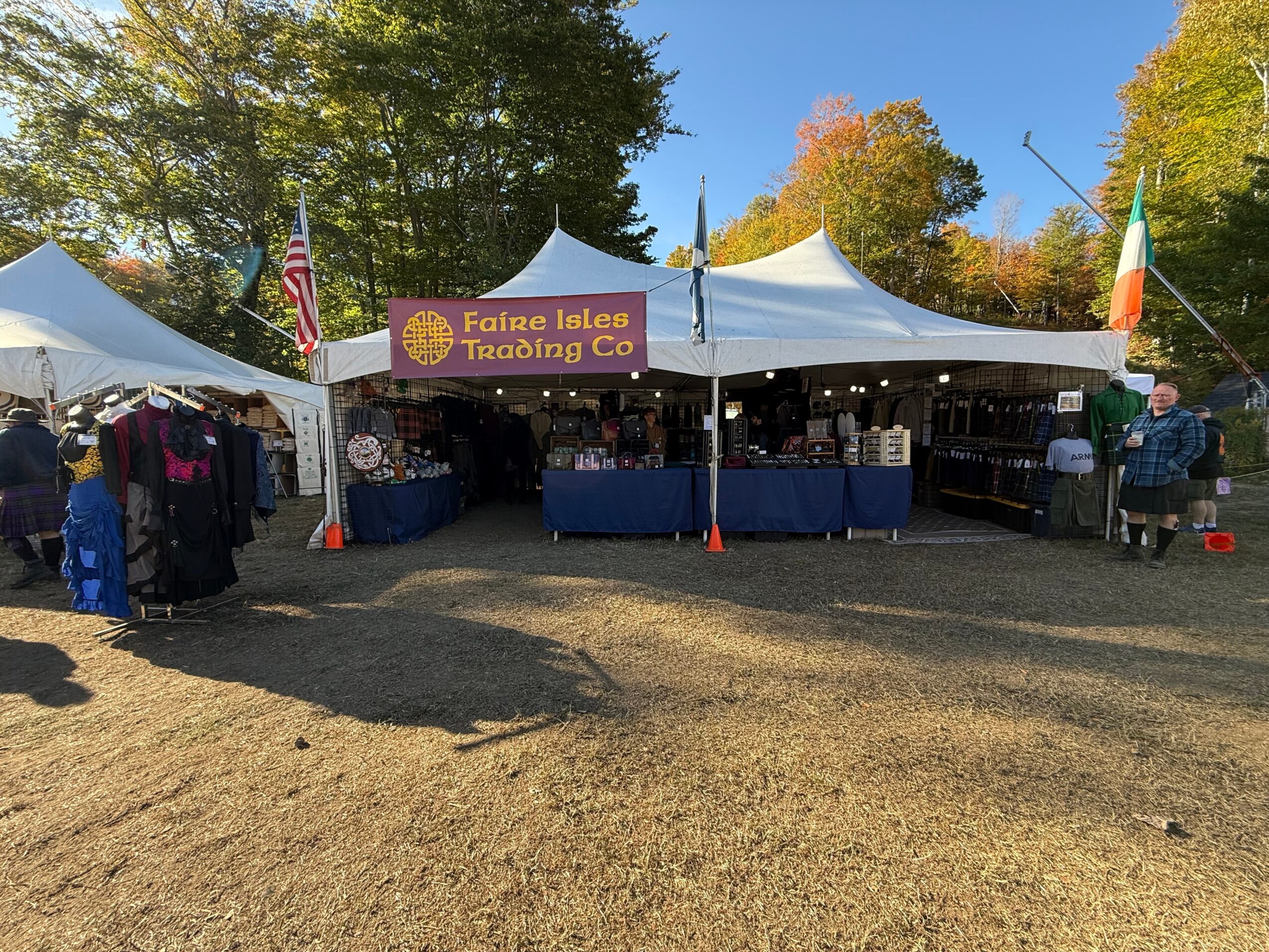 Fairie Isles Trading Co. booth with tents, tables, and people outdoors on a sunny day, trees in background.