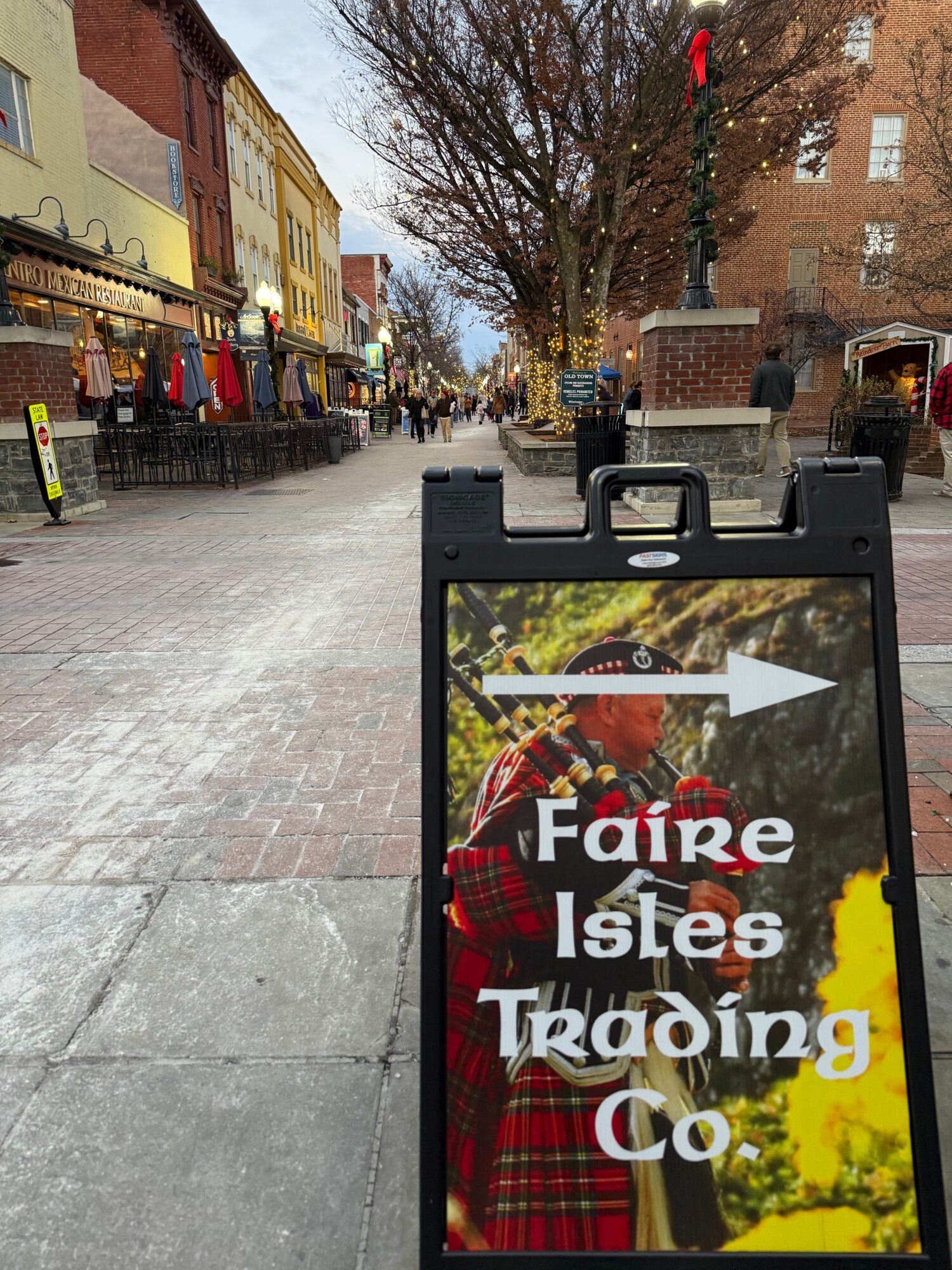 Street scene with a sidewalk, trees, and buildings, and a digital signboard displaying text and graphics, viewed sideways.