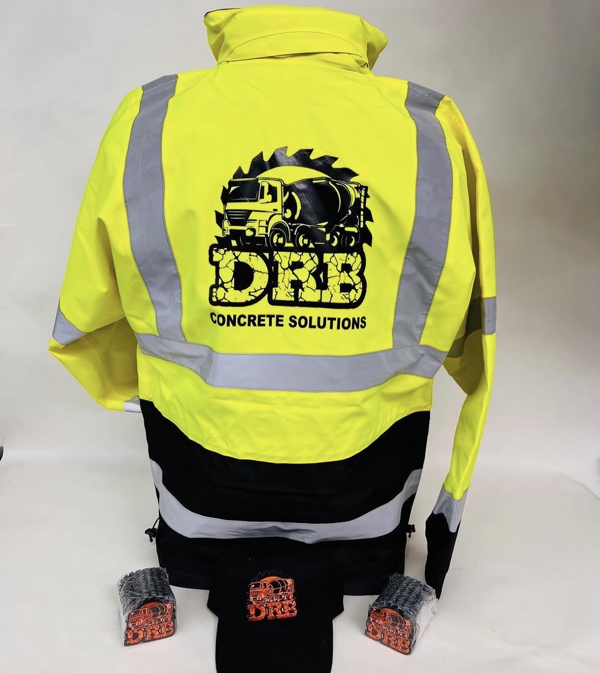 Back view of a high-visibility yellow jacket with reflective stripes and a logo for concrete solutions, with black and white accents.