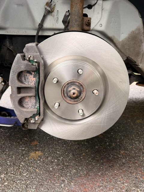 Car brake disc and caliper assembly, viewed from front, on a textured surface.