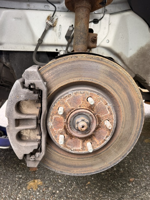 Car brake disc and caliper assembly with rust and dirt, viewed from the side.