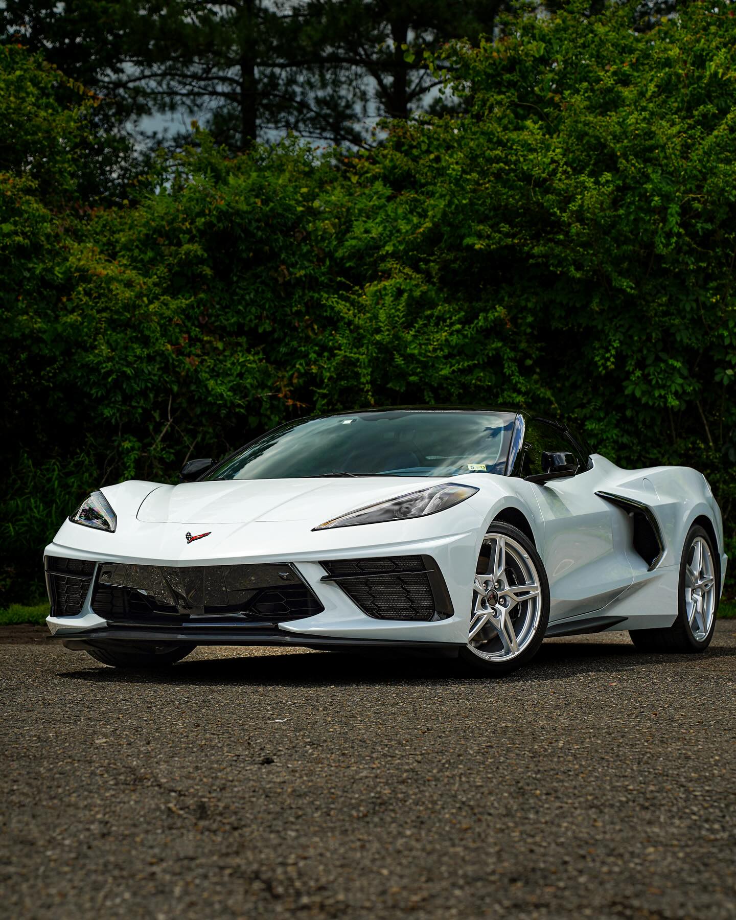 White sports car parked on a road with green trees in the background.
