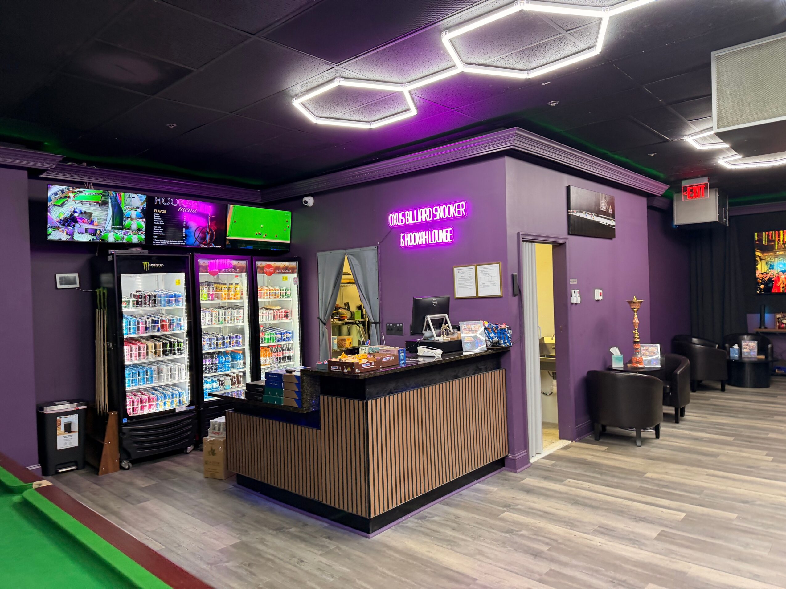 Reception area with purple walls, a counter, vending machines, and seating, illuminated by modern ceiling lights.