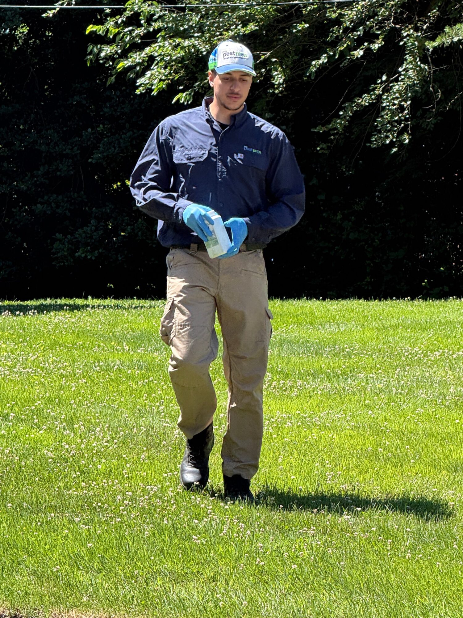 Person in a dark jacket, beige pants, and a cap holding a golf club on a grassy field.