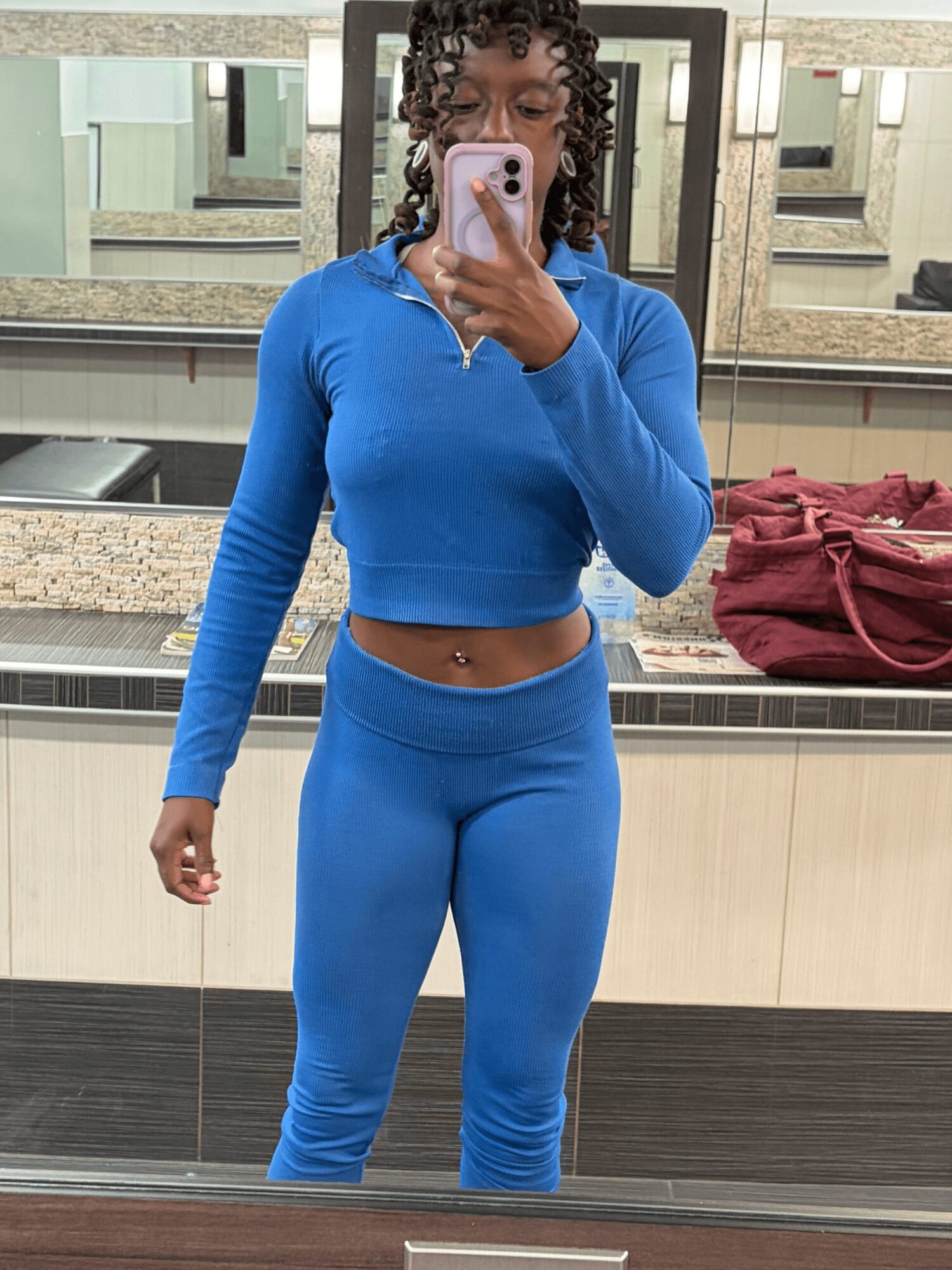 Person taking a mirror selfie in a bathroom, wearing a blue athletic outfit, with a mirror and sink in the background.