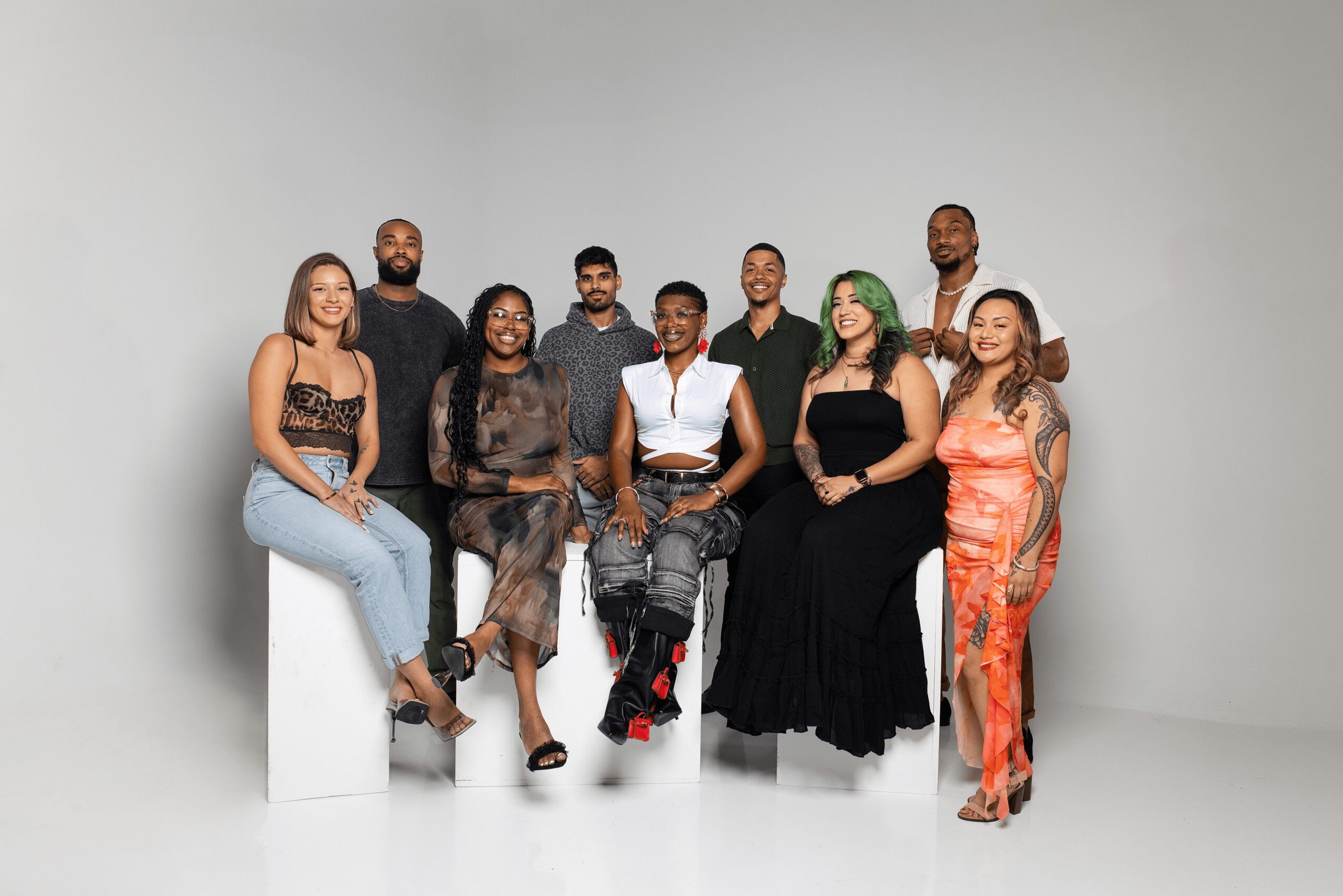 Group of ten diverse people posing together in a studio with a plain background.