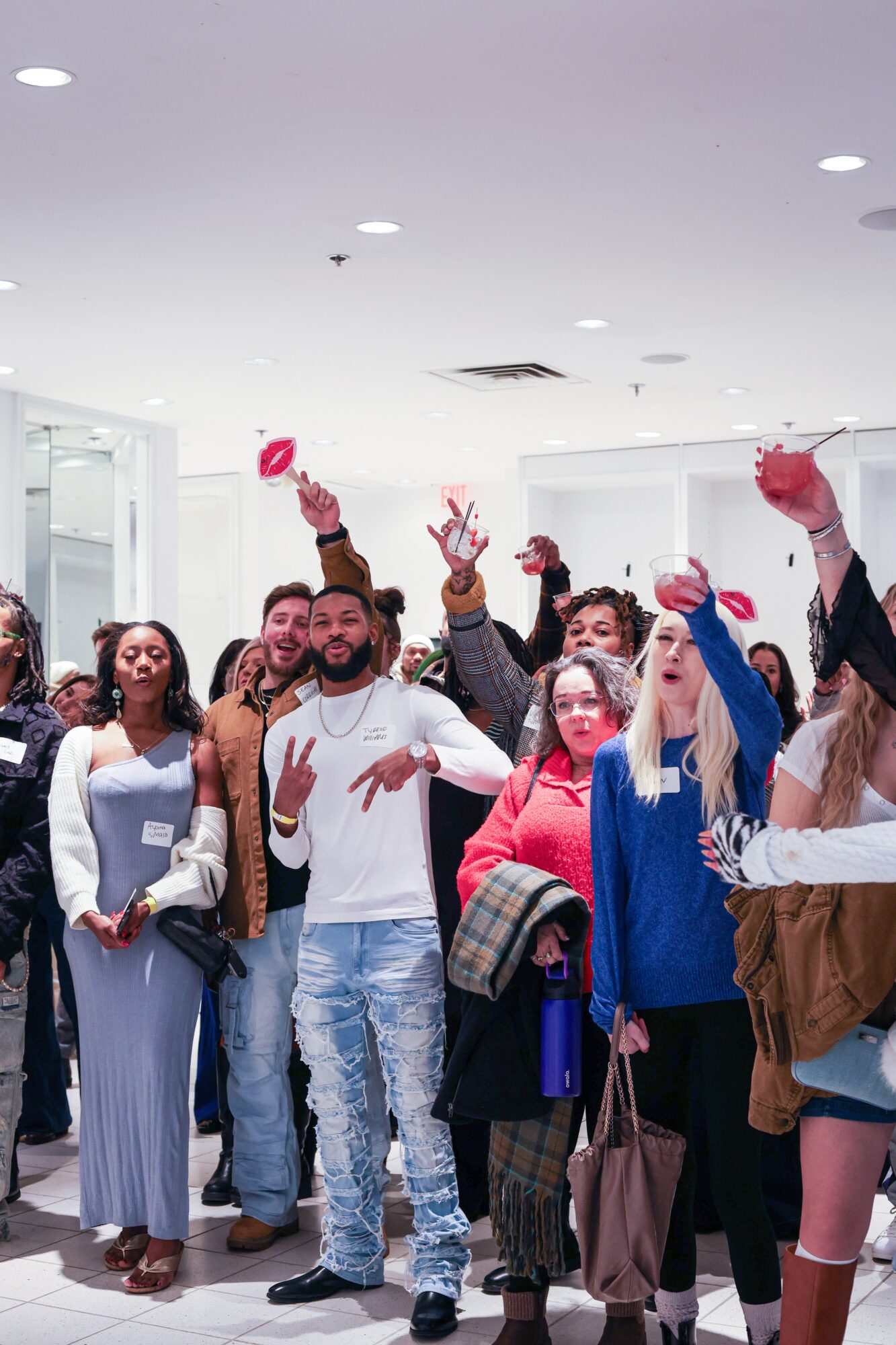Group of people gathered indoors, some raising hands, smiling, and holding pink balloons, in a bright, modern space.