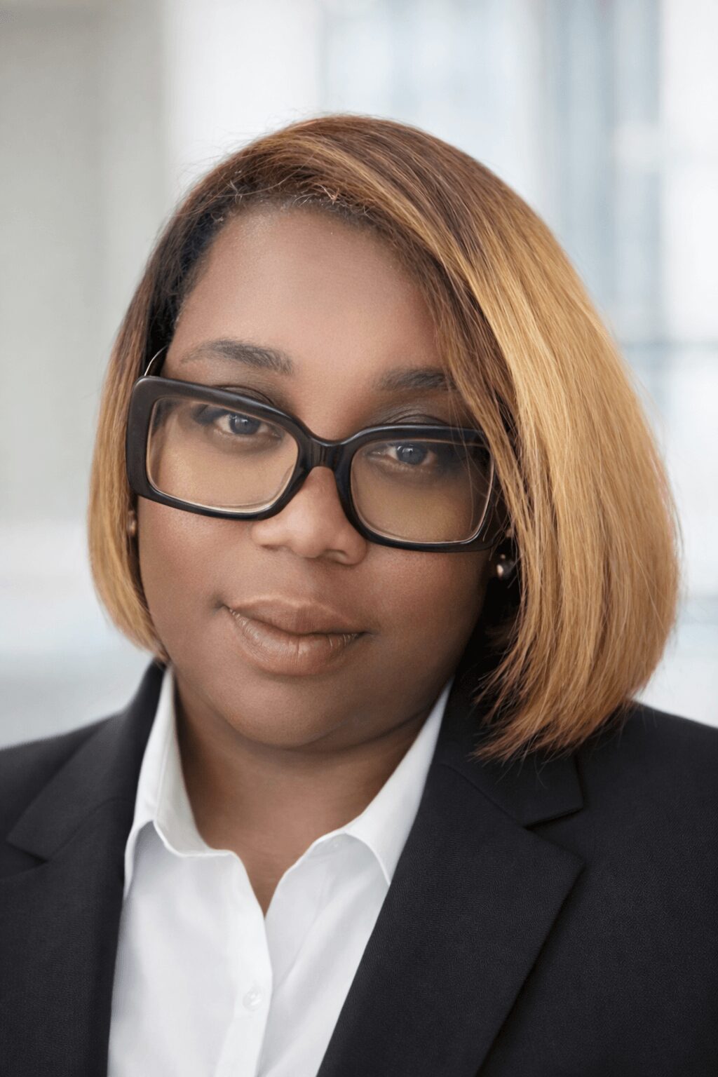 Professional woman with shoulder-length hair, glasses, wearing a black blazer and white shirt, in an office setting.