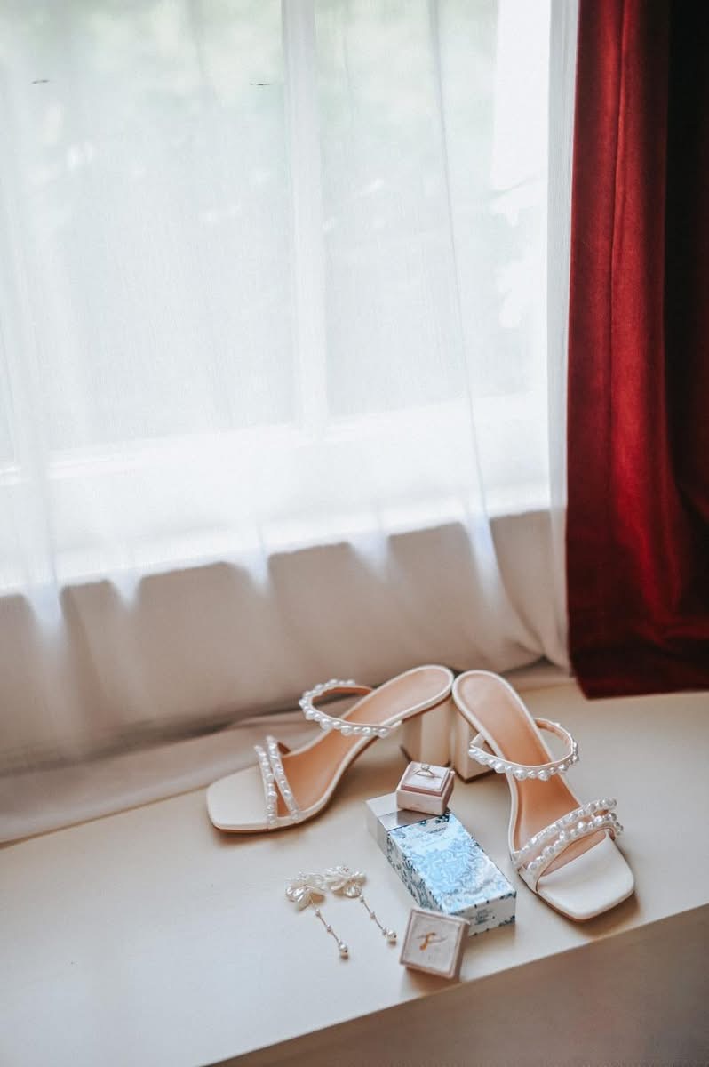 High-heeled shoes, jewelry, and a small box on a windowsill with curtains in the background.