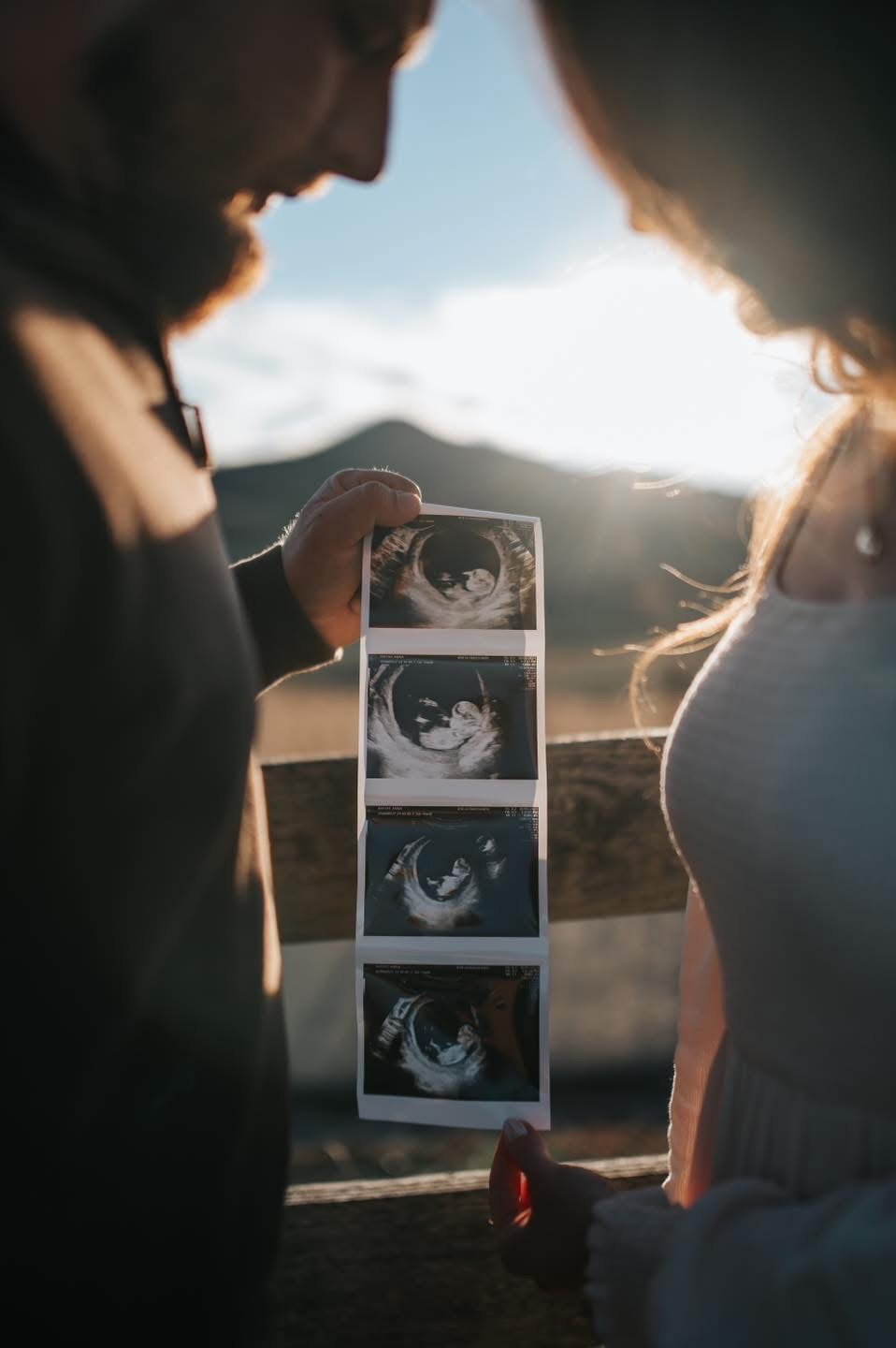Two women look at ultrasound images outdoors with sunlight behind them, holding a strip of ultrasound photos.