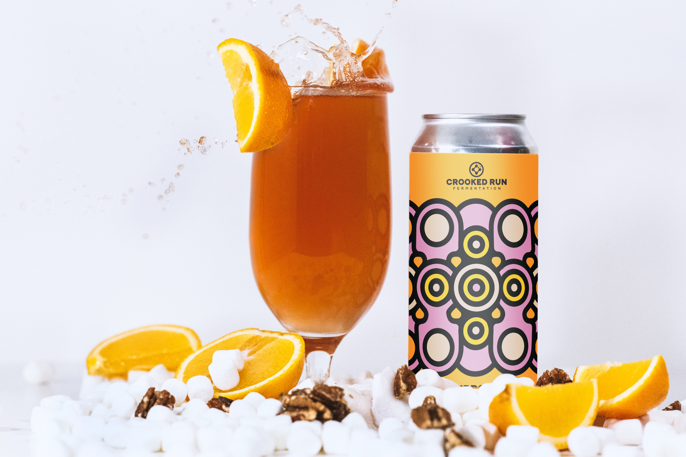 A tall glass with orange drink and lemon wedge, next to a can with colorful circular pattern, and lemon slices.