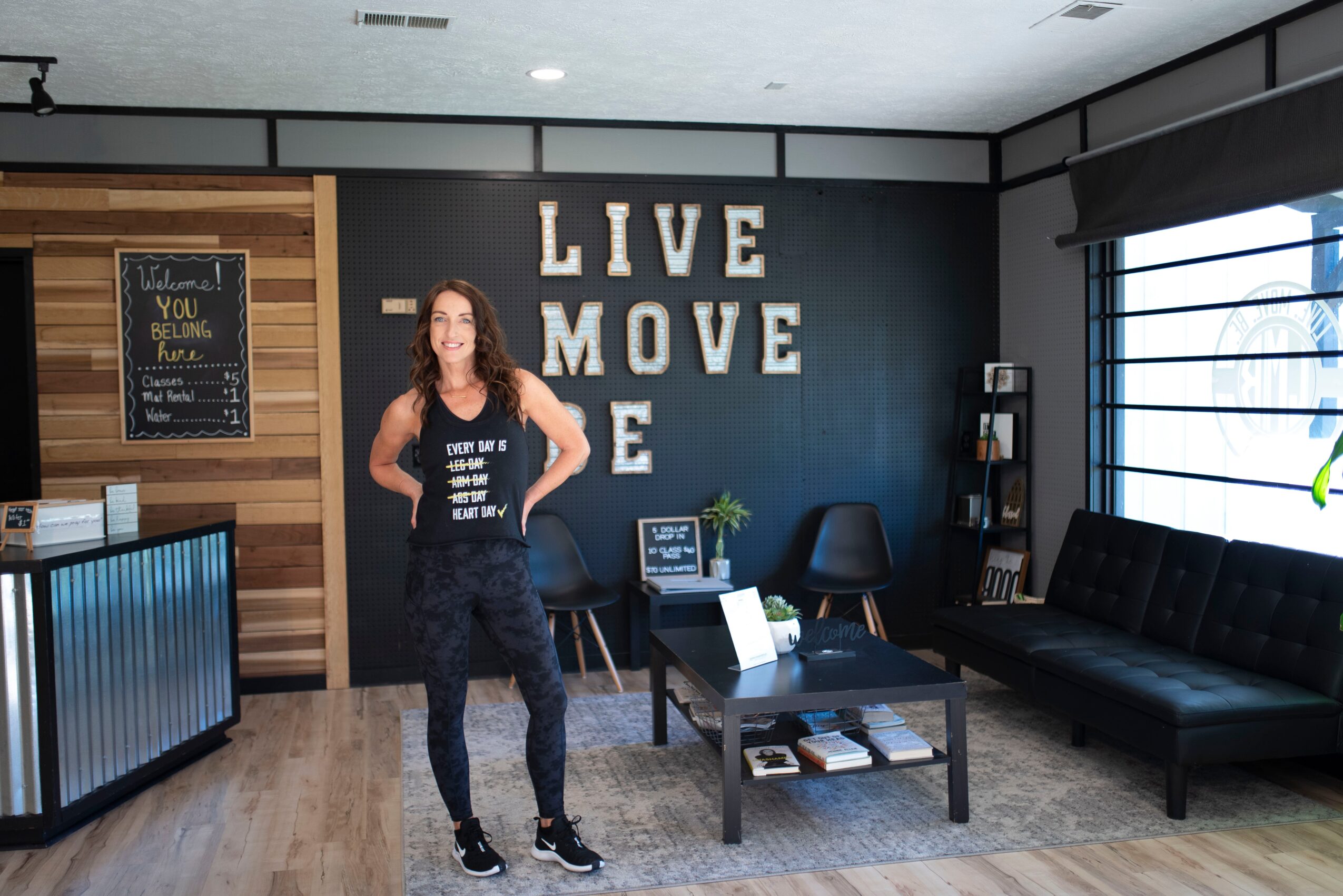 Woman standing in a modern room with a black wall, large white letters saying 'LIVE MOVE LOVE', and furniture.